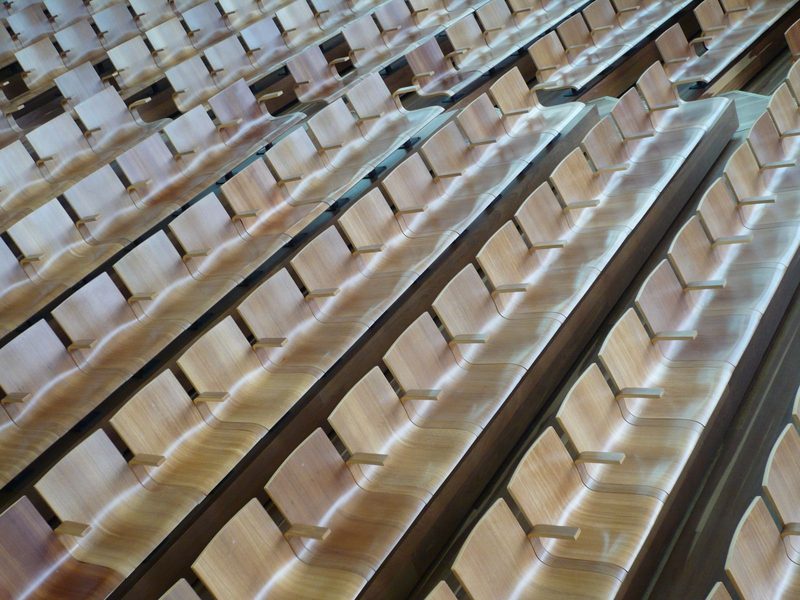 Rows of empty folding seats in a lecture hall, in ink duotone.